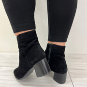 Black high-heeled boots worn with black leggings on a light wooden floor.