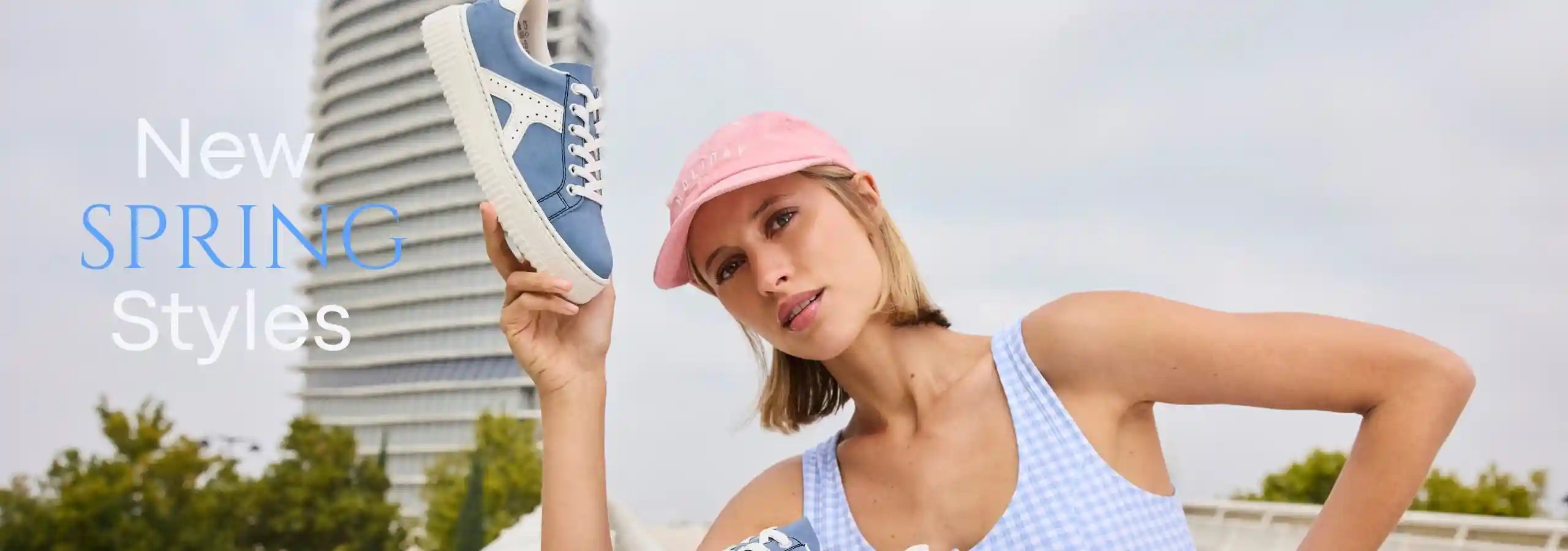 Woman wearing a pink cap and light blue top with text 'New Spring Styles' on a blurred outdoor background